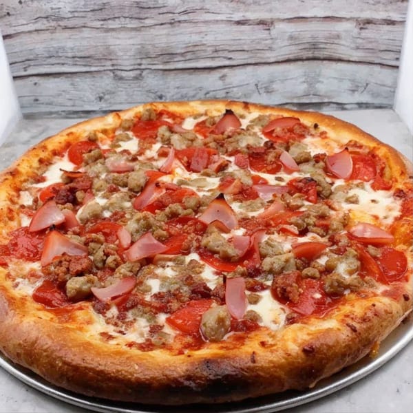 Partners II Pizza's meat lover's pizza with pepperoni, sausage, and ham on a metal pan.