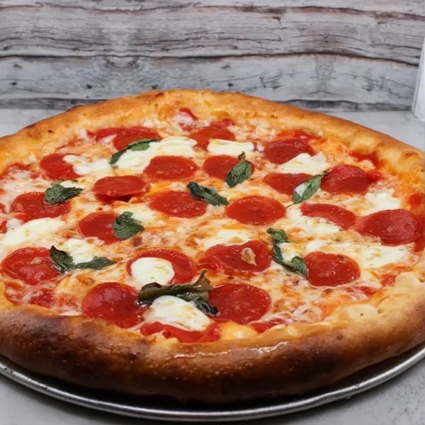 A Partners II Pizza pepperoni pizza with fresh mozzarella and basil on a metal pan.